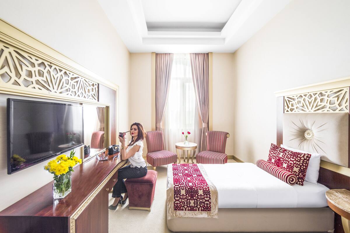 Habitación de hotel con cama, televisor, escritorio con un jarrón de flores y dos sillones.