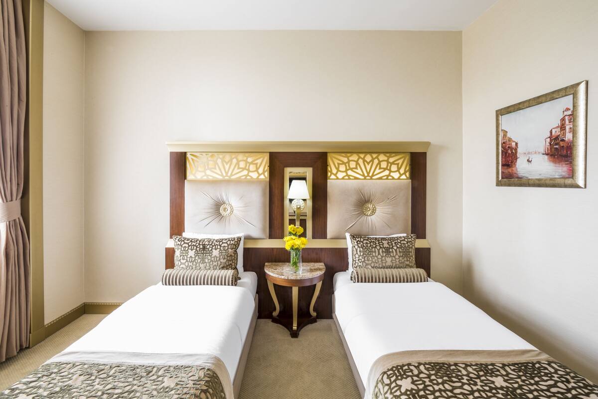 Habitación de hotel con dos camas, una mesita con un florero, un espejo y un cuadro en la pared.