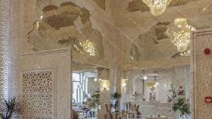 Un vestíbulo lujoso con un sofá, dos mesas redondas, un techo ornamentado y candelabros.