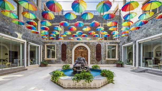 Un patio con una fuente, rodeado por un muro de piedra y puertas de cristal.