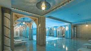 Un vestíbulo amplio con columnas de mármol, una zona de piscina y un techo con diseños intrincados.