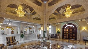 Un amplio vestíbulo con candelabros, techo ricamente decorado y una recepción.