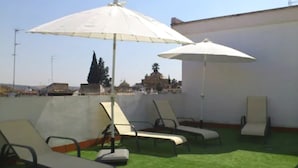 A rooftop terrace with lounge chairs and umbrellas, offering a view of buildings and trees. - Apartamentos La Fuente (Córdoba)