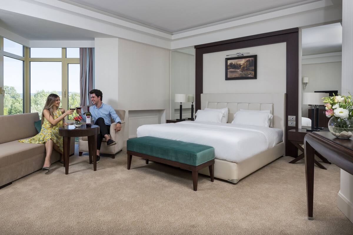 Habitación de hotel con una cama grande, un sofá, una mesita y vistas al exterior.