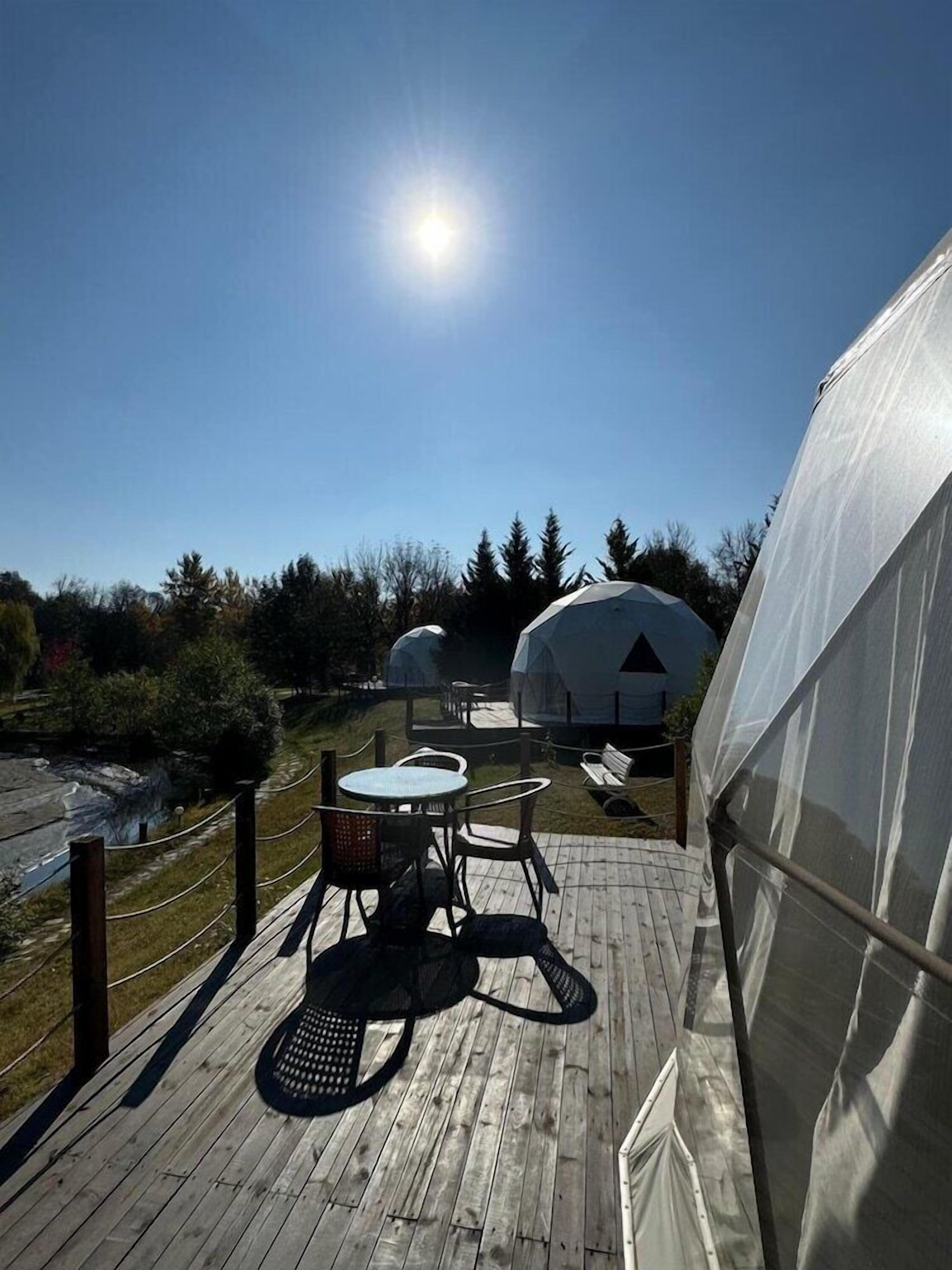 A wooden deck with a table and chairs, a covered seating area, and a large dome structure.