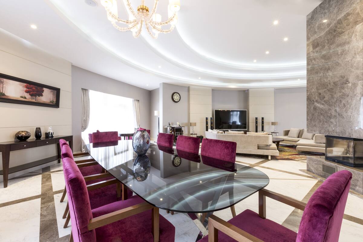 Una sala de estar moderna con una mesa de comedor de vidrio, sillas moradas, un sofá y un televisor.