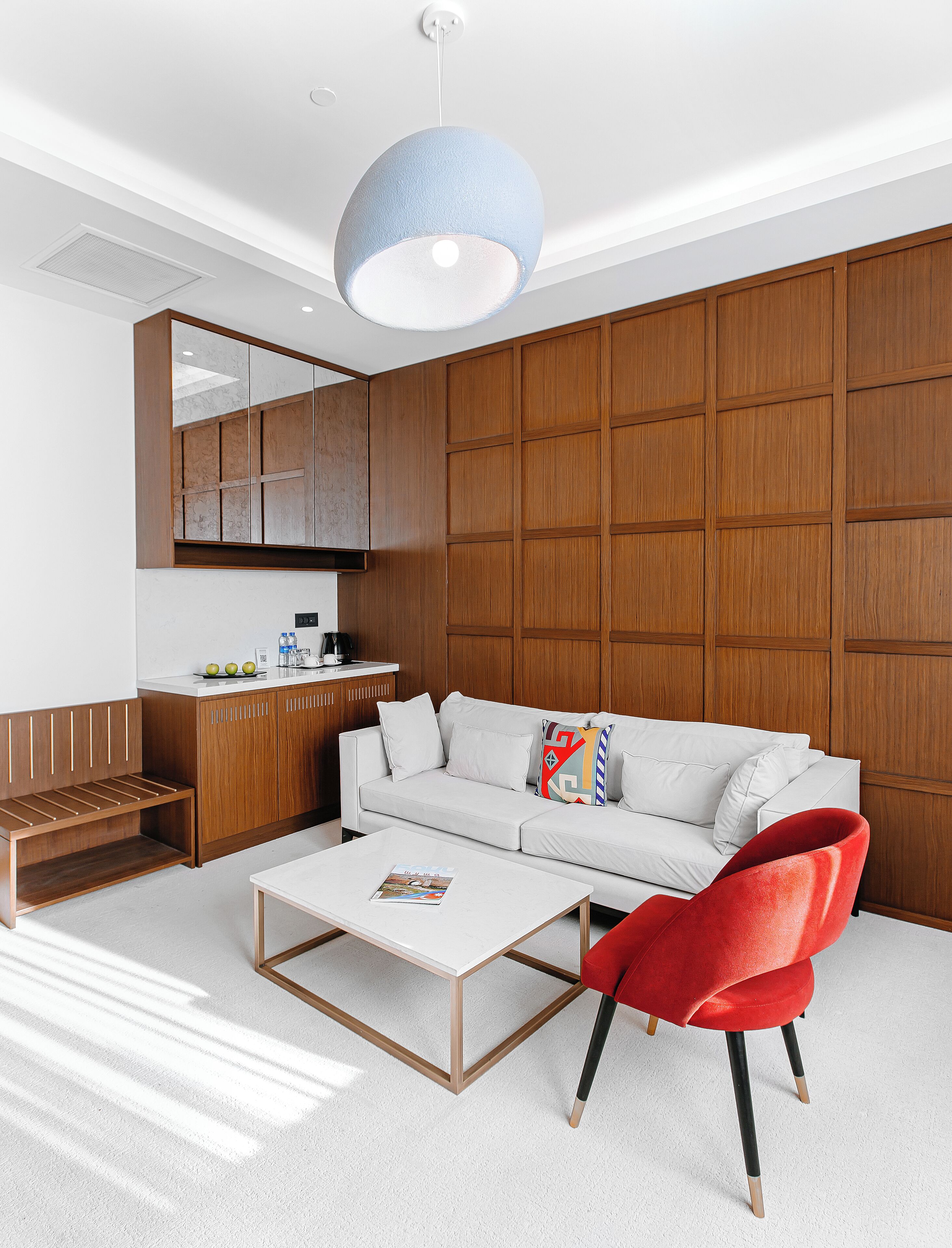 A modern living room with a white sofa, a red chair, and a coffee table.