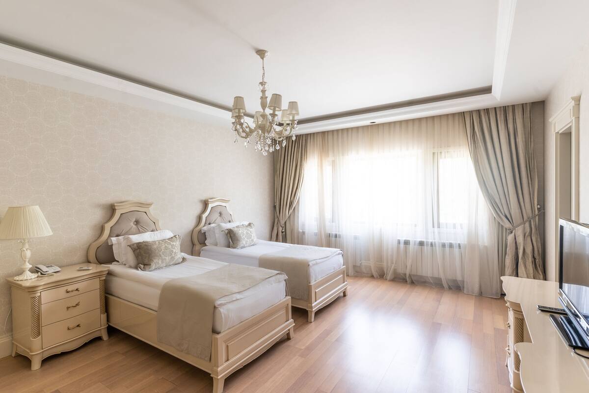 A bedroom with two beds, a nightstand, a TV, and a chandelier.