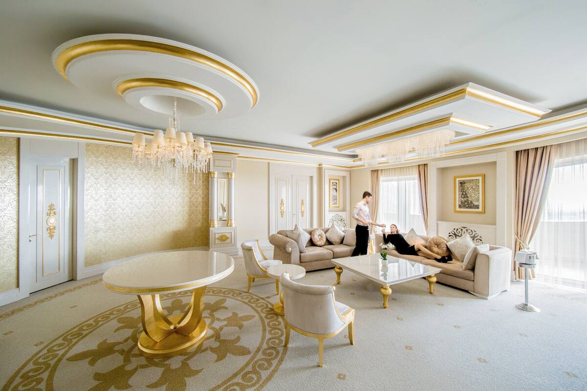 A luxurious living room with a round gold table, beige sofas, and a chandelier.