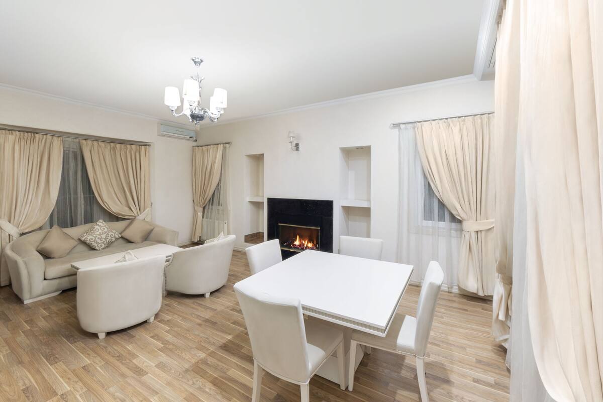 A modern living room with a white sofa set, a white dining table, and a fireplace.