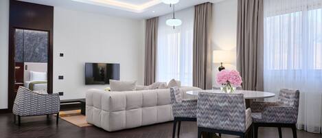 A modern living room with a sofa, dining table, chairs, a TV, and a large window with curtains.