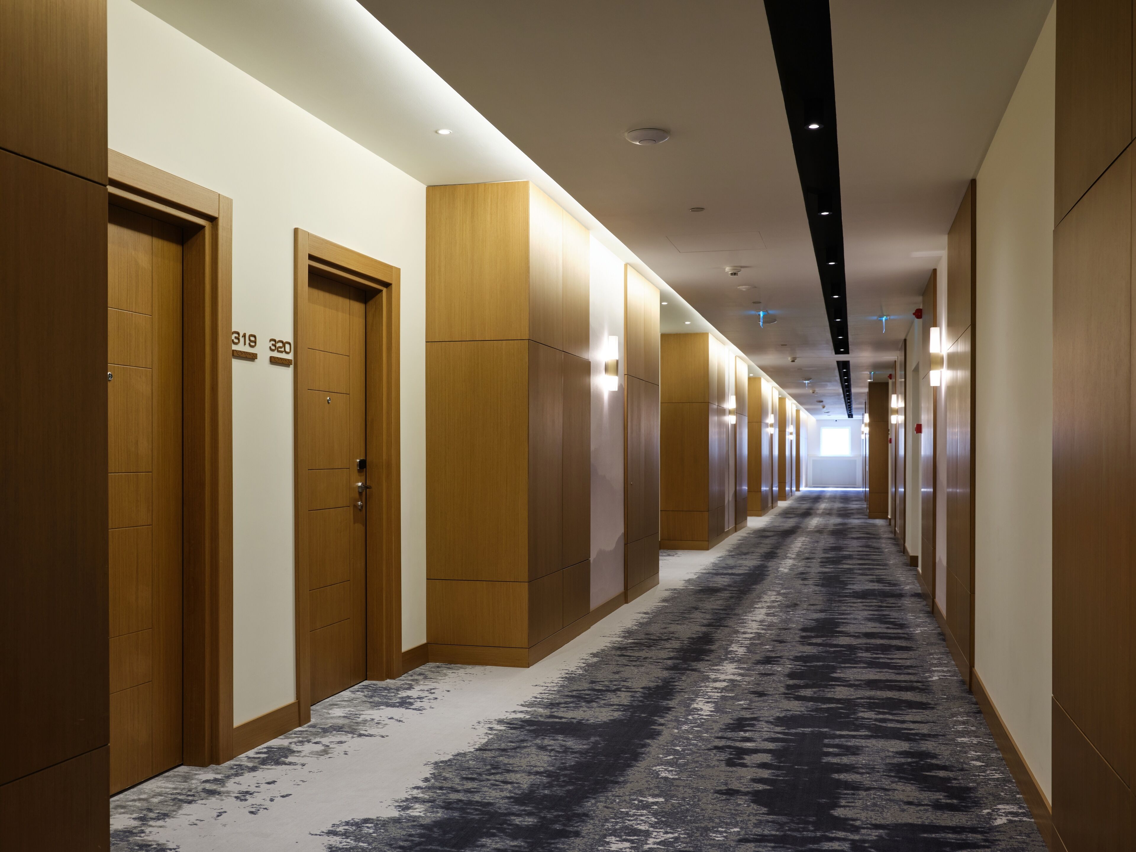 A long, narrow hotel corridor with wooden doors and a patterned carpet.