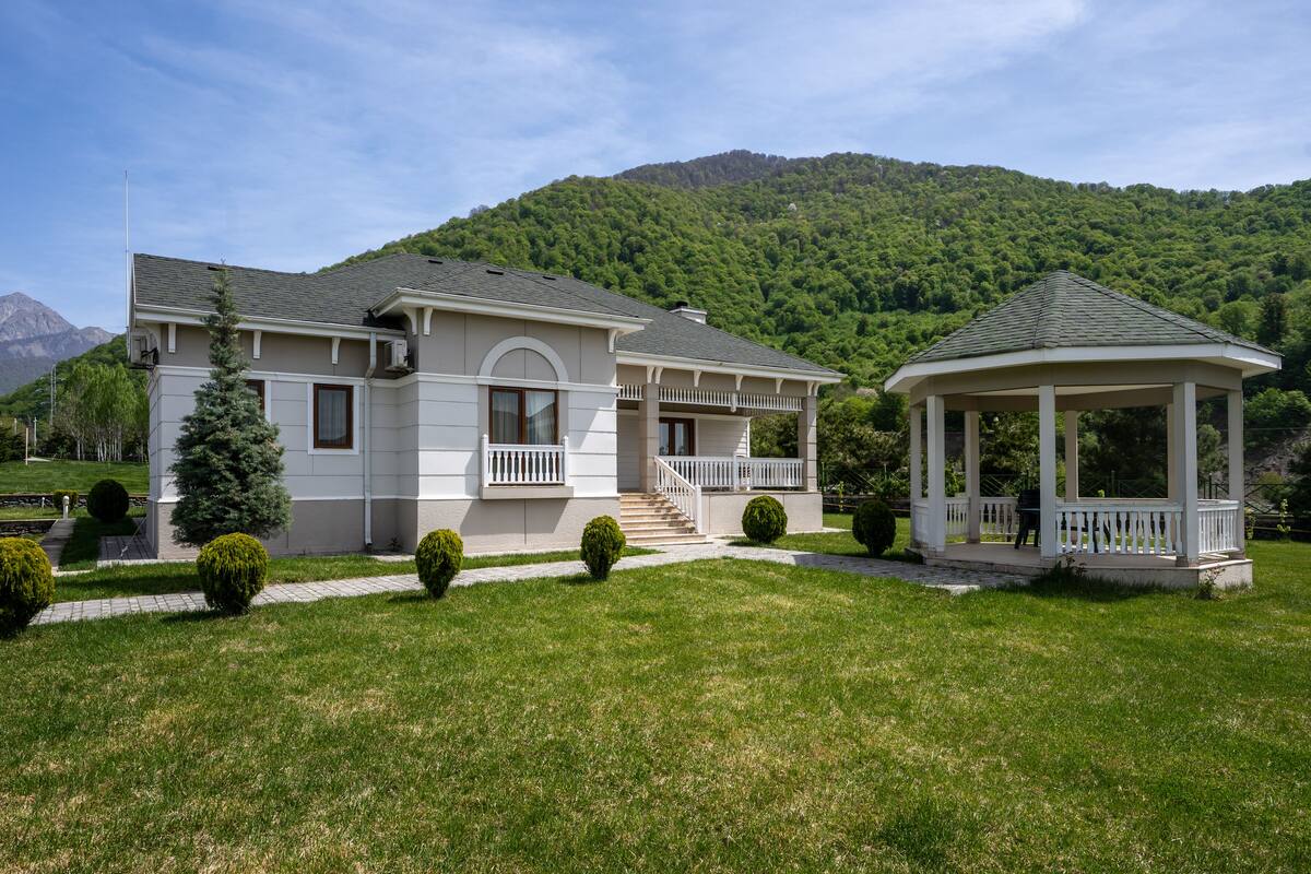 A two-story house with a balcony, a gazebo, and a mountain backdrop.