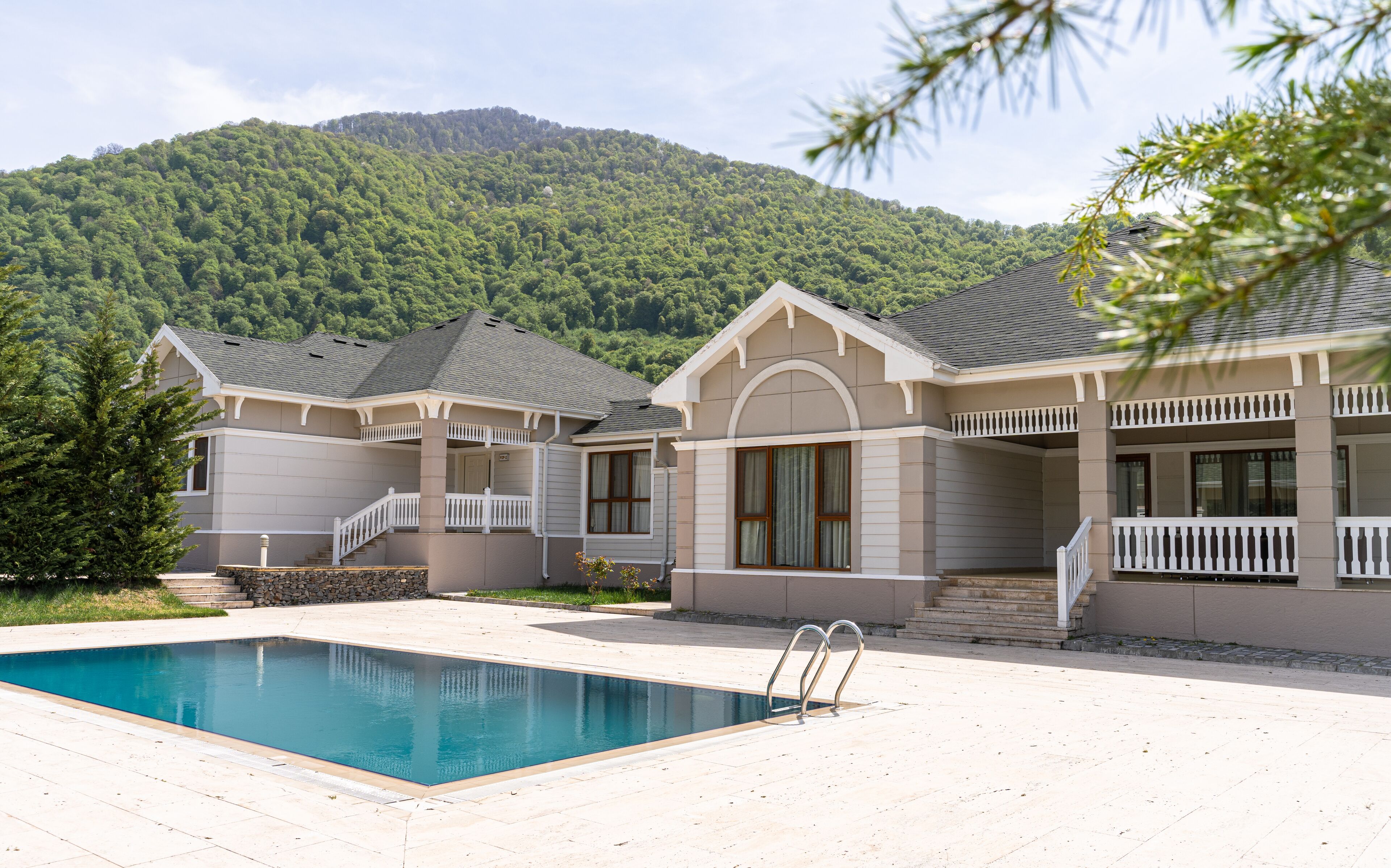 Una casa de dos pisos con piscina, con montañas al fondo.
