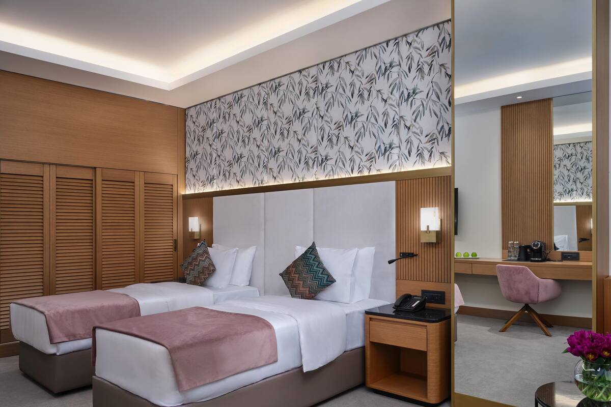 A hotel room with two beds, a desk, a chair, a mirror, and a wall with a leaf pattern.