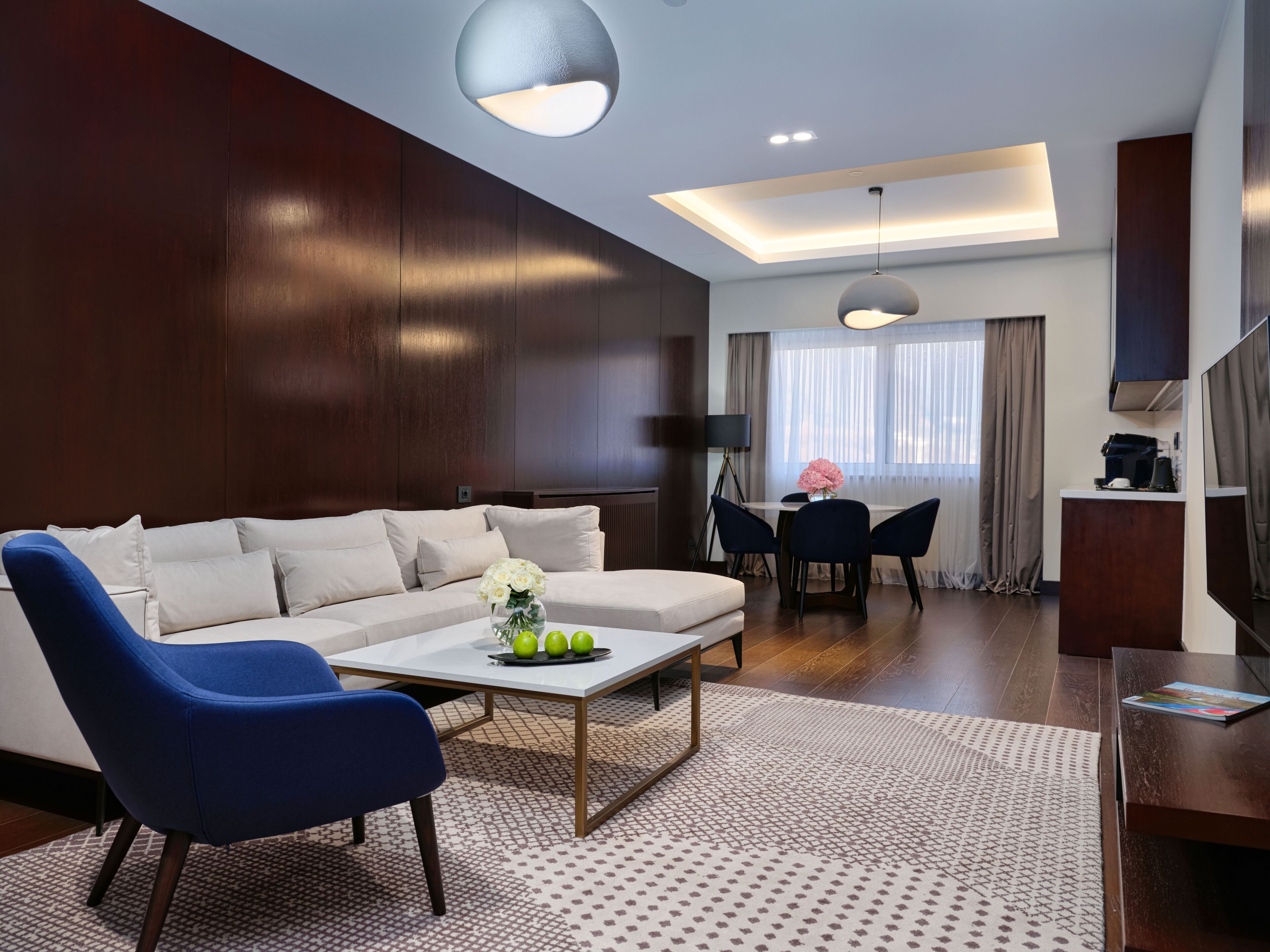 A modern living room with a sofa, blue armchair, coffee table, and dining area with a table and chairs.