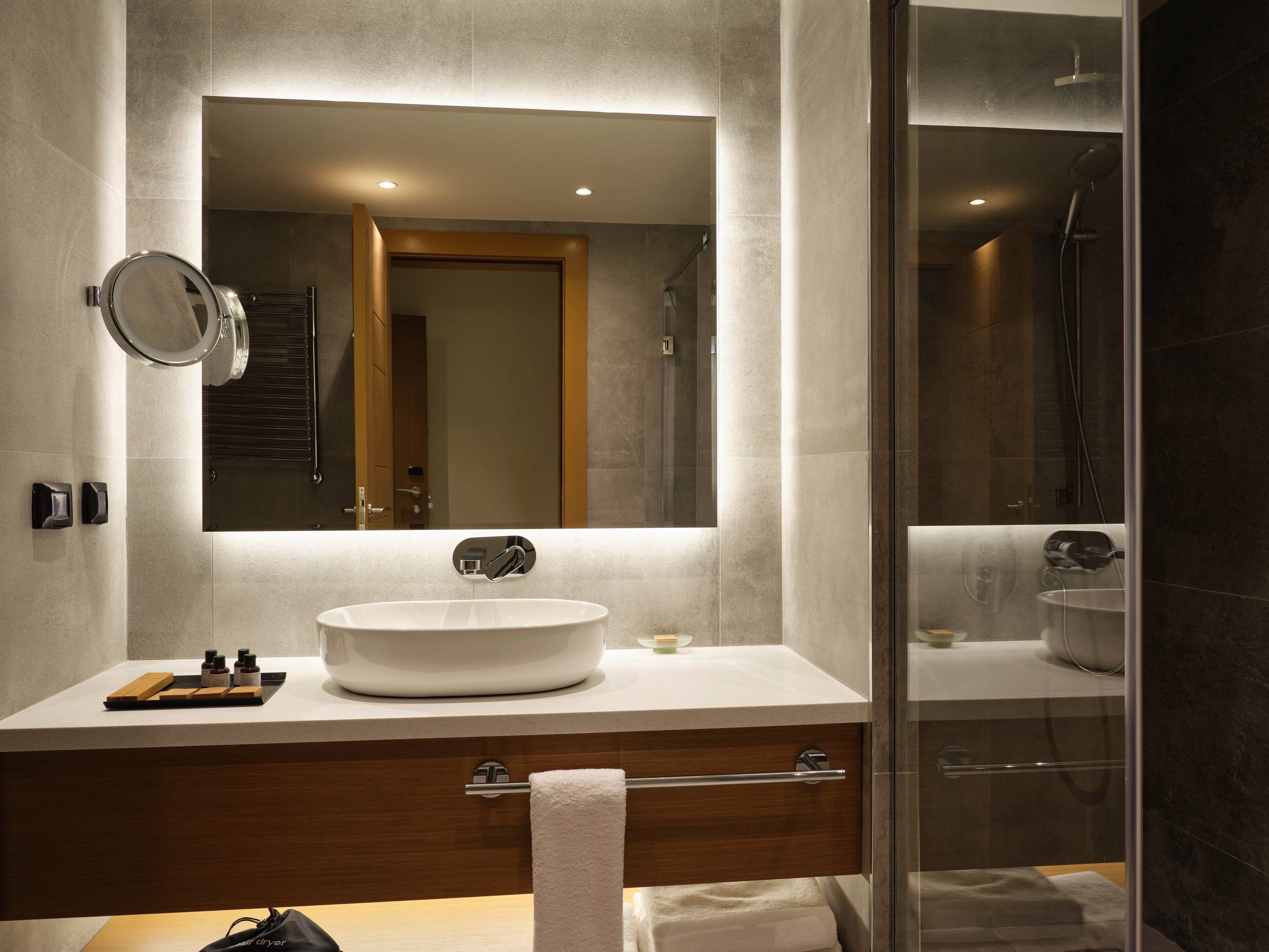 A modern bathroom with a large mirror, a round sink, a towel rack, and a glass shower enclosure.