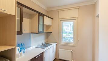 A compact kitchen with a built-in sink, a window with a view of a stone wall and a house, and a radiator.