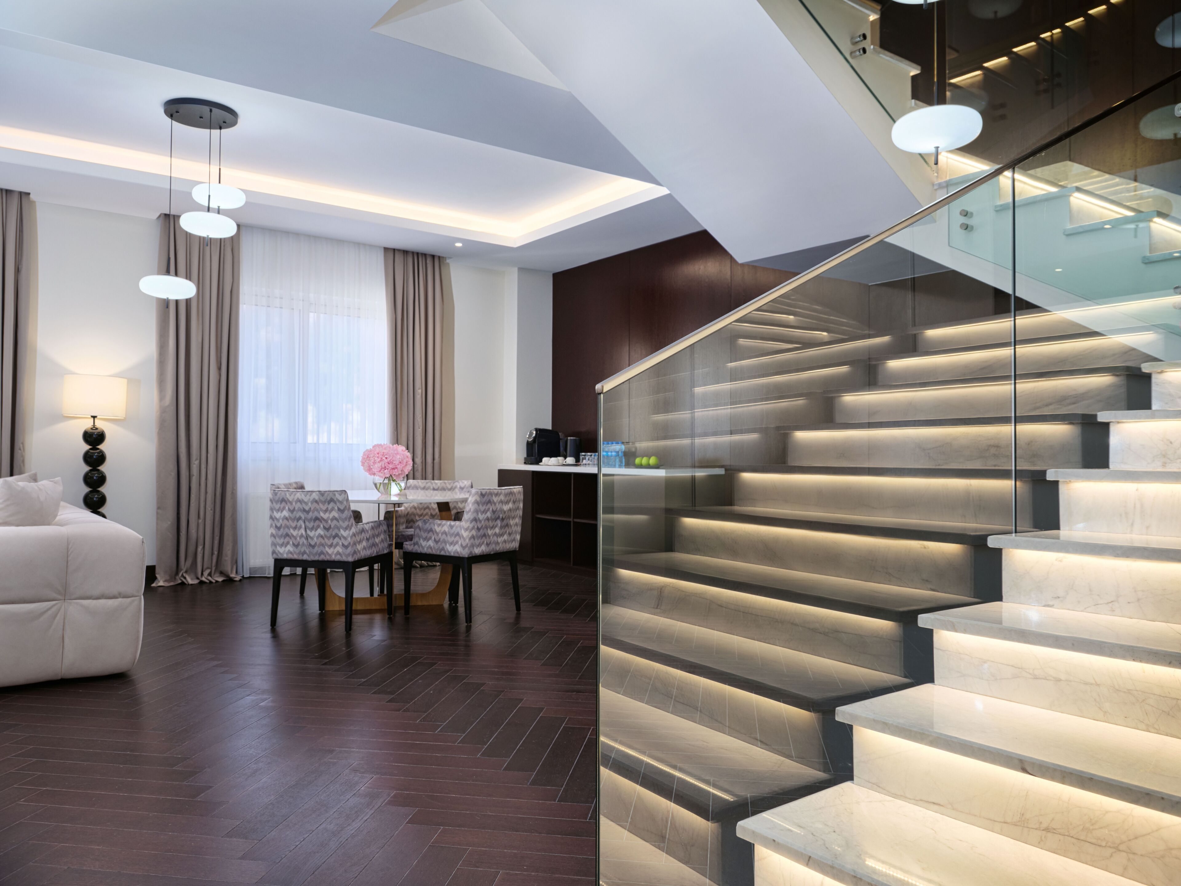 A modern hotel room with a marble staircase, a dining area with a table and chairs, and a sofa.