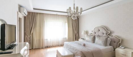 A bedroom with a large bed, bedside tables, a TV, and a chandelier.