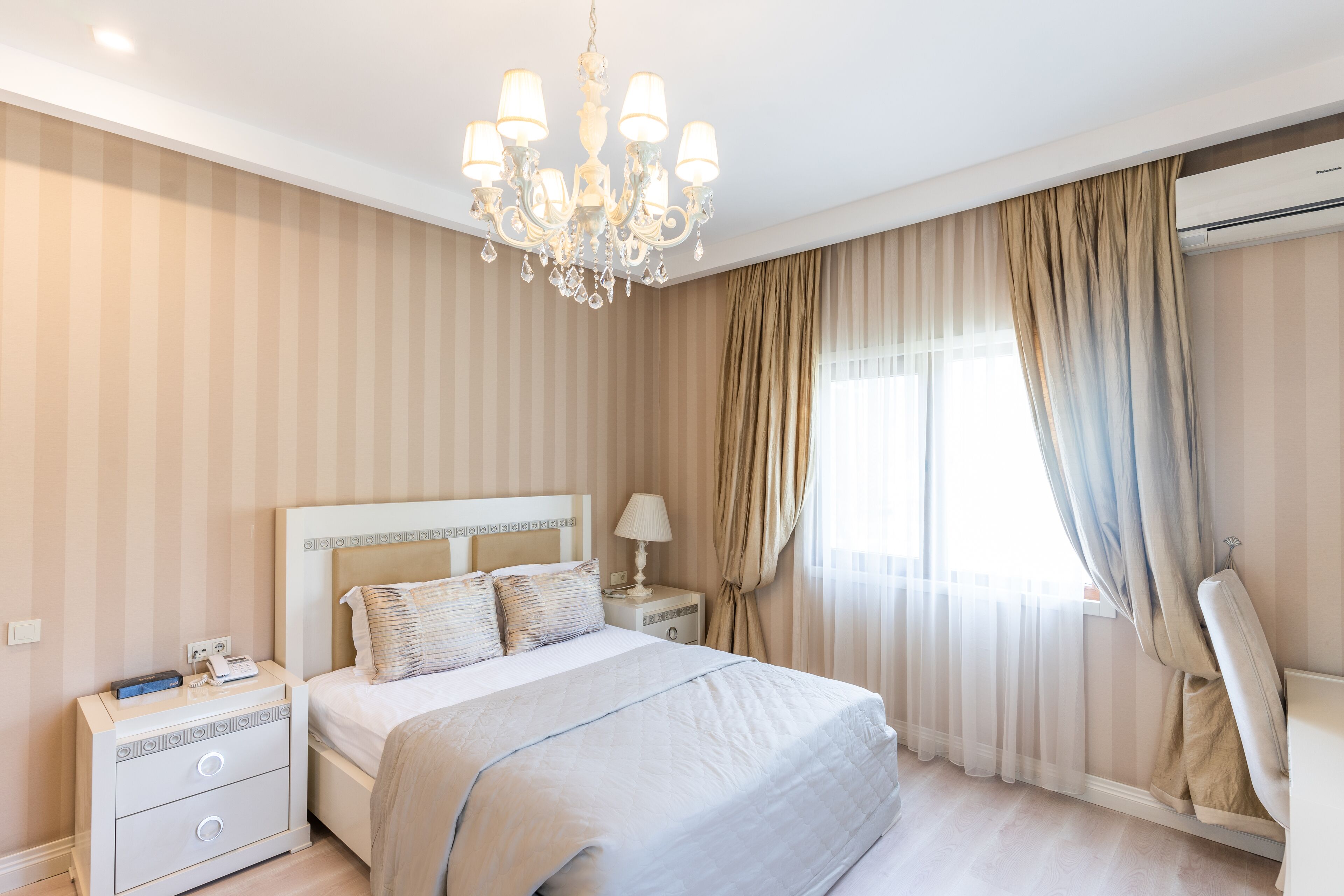 Habitación de hotel con una cama grande, una mesita de noche, una lámpara, una silla y un ventanal con cortinas.