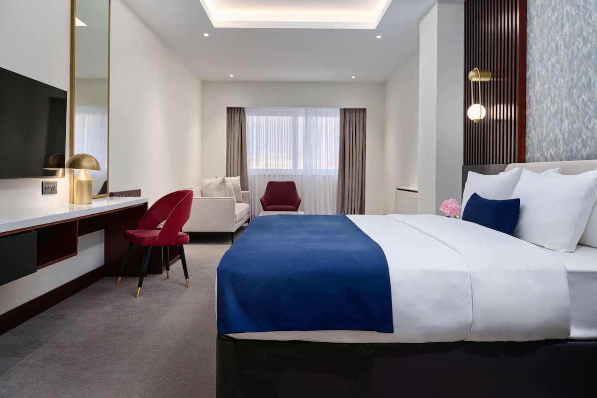 A hotel room with a bed, a desk, a chair, a large mirror, and a window with curtains.