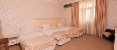 A hotel room with two beds, a chandelier, a large window with curtains, and a wooden chair.
