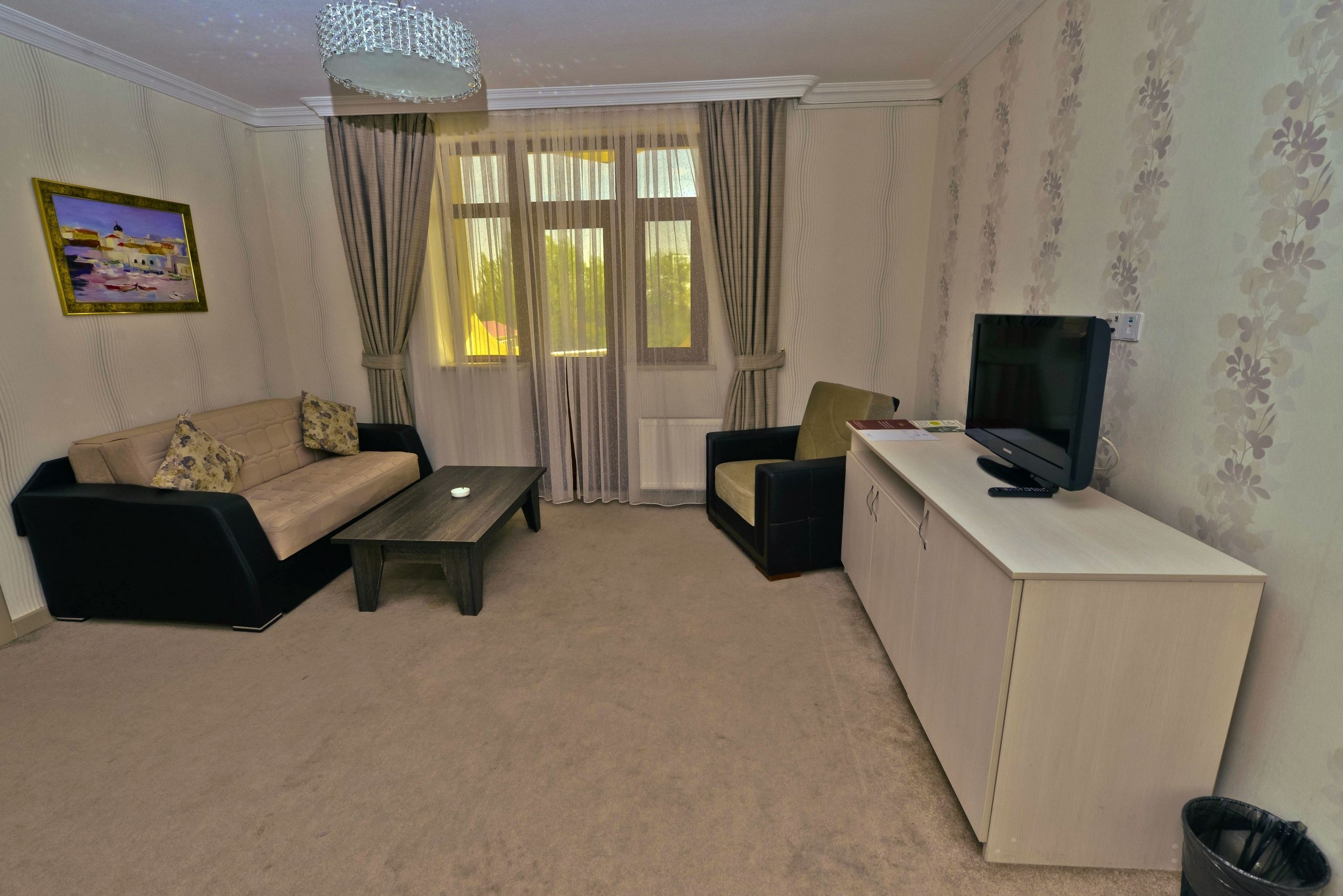 Una sala de estar con sofá, una mesa de centro, televisor sobre un mueble y una ventana con cortinas.