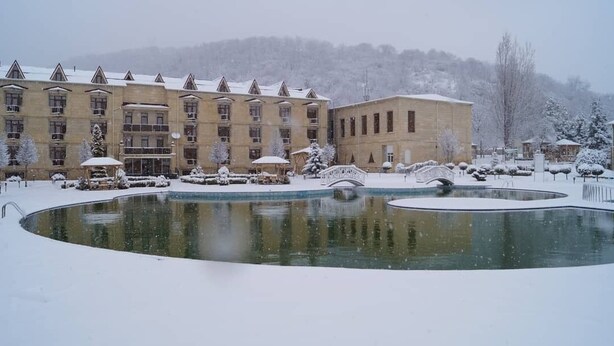 A snow-covered courtyard with a pool, a bridge, and a building with multiple floors and balconies. -  Qebele Yeddı Gozel Hotel (Gabala)