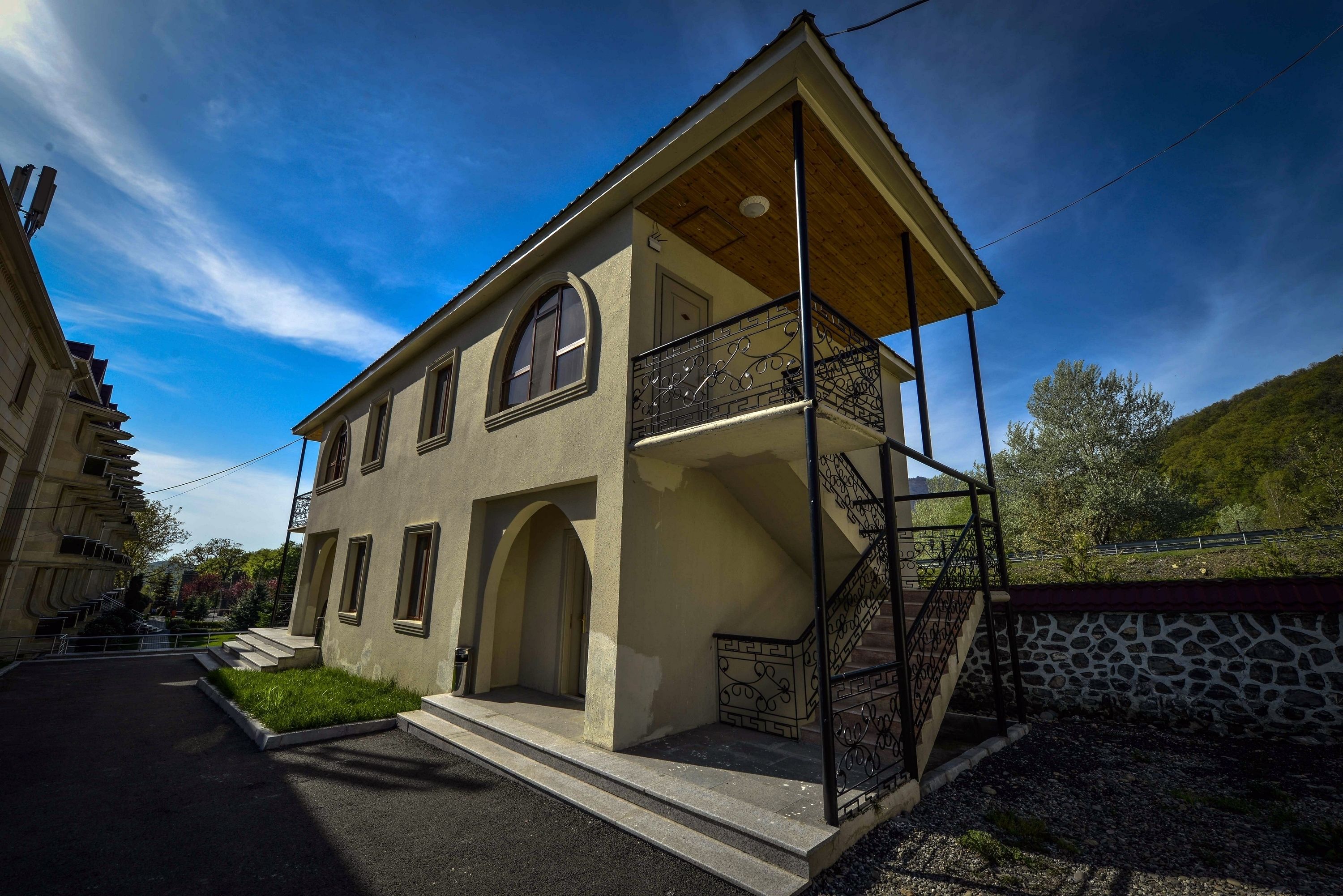 A two-story building with a balcony, a staircase, and a stone wall.