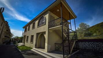 A two-story building with a balcony, a staircase, and a stone wall.