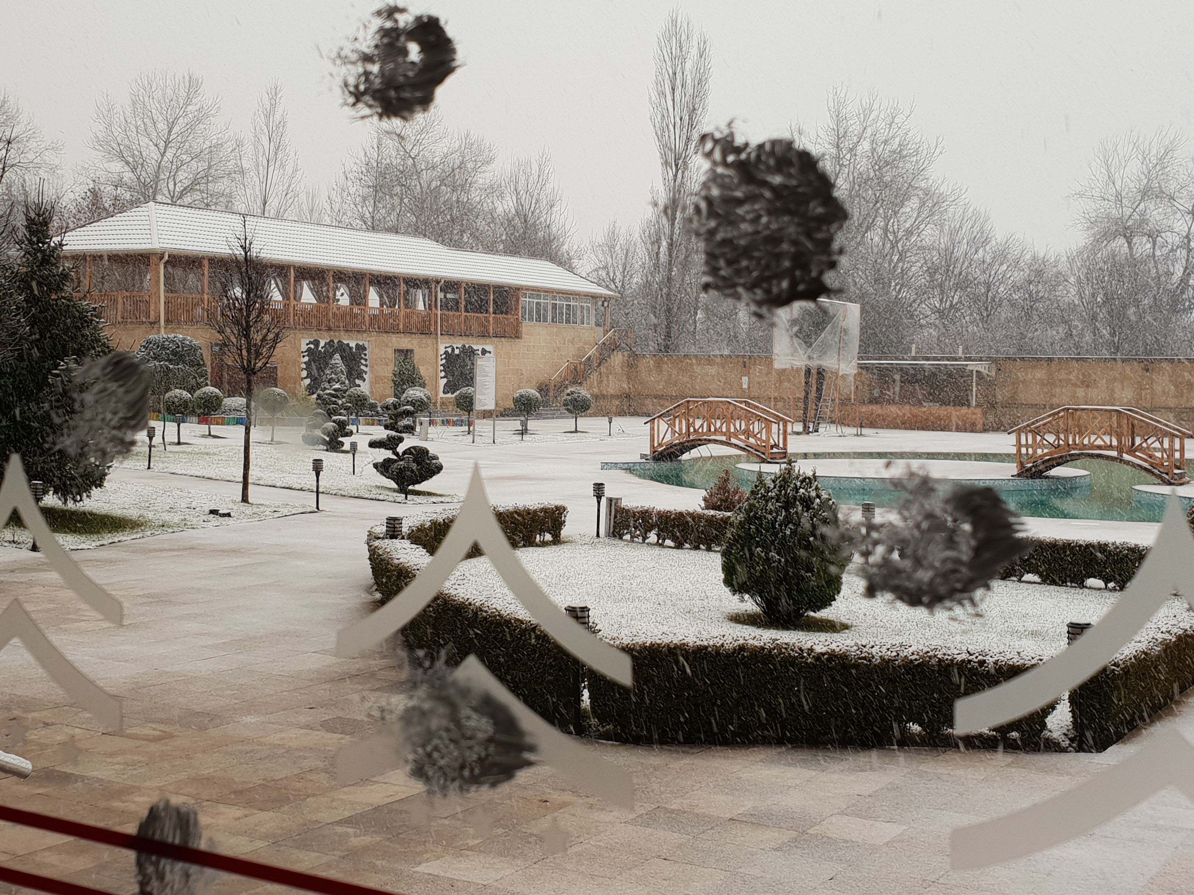 A snow-covered courtyard with a gazebo, a bridge, and a pool.