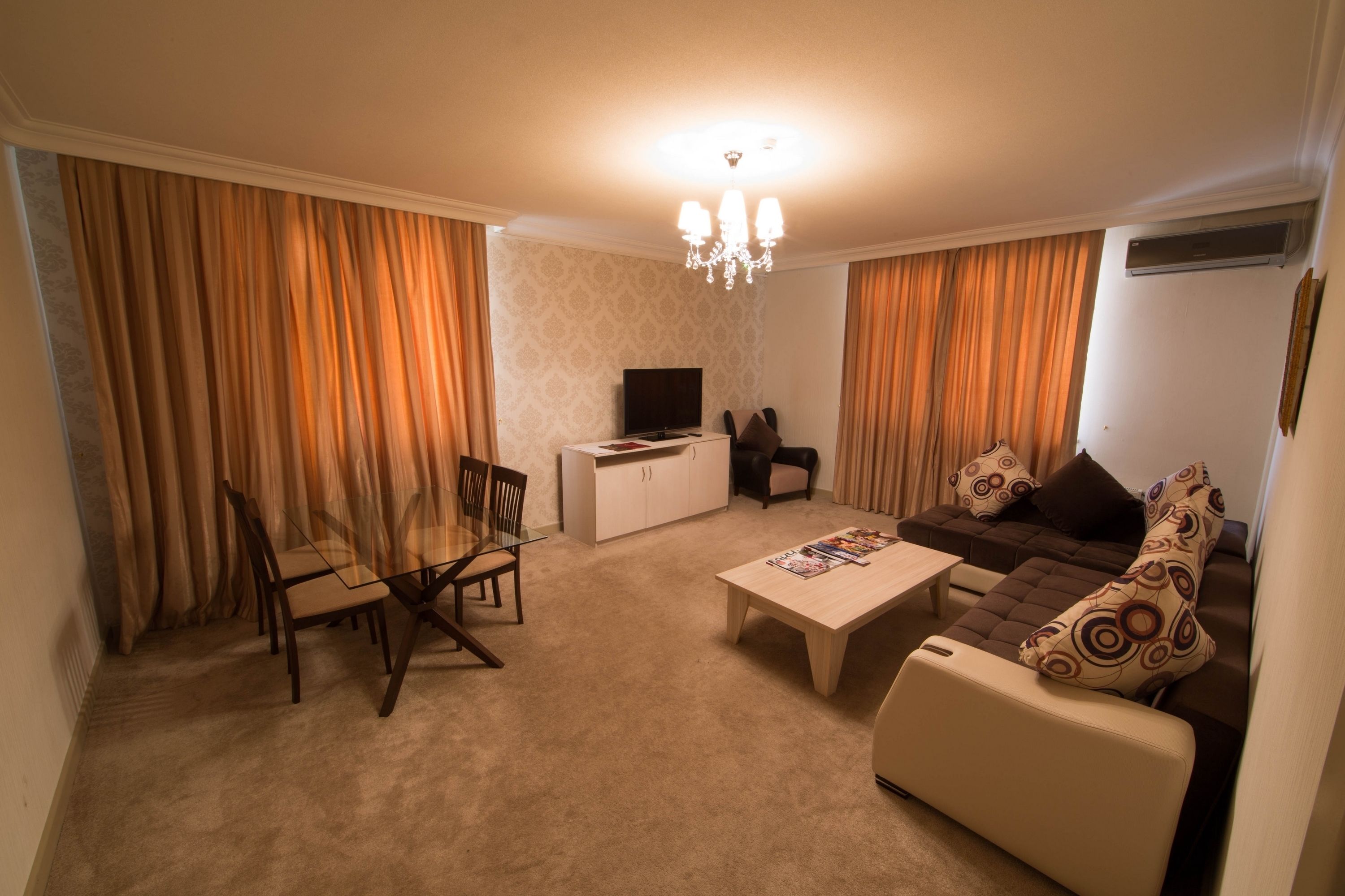 A living room with a sofa, a coffee table, a TV, and a dining area with chairs and a table.
