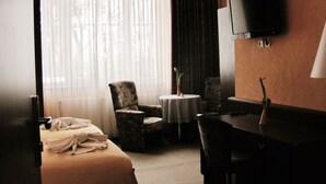 Une chambre d’hôtel comprenant un lit, un bureau, une chaise, une petite table avec un vase et un téléviseur fixé au mur.