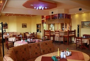 Un restaurante con mesas redondas, sillas de madera y una zona central con sofás.