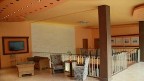 Un hall d’entrée spacieux avec un plafond haut, un téléviseur fixé au mur et un coin salon doté de meubles en osier et d’une table en marbre.