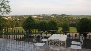 Une terrasse avec une table et des chaises, donnant sur un paysage rural avec des arbres et des maisons.