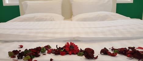 Un letto con biancheria e cuscini bianchi, una parete verde e una finestra sullo sfondo.