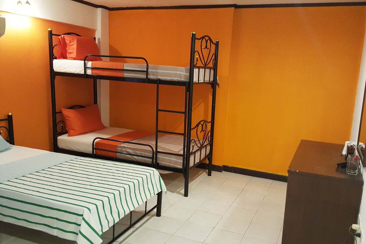 A bunk bed room with orange walls, a desk, and a bed with a striped bedspread.
