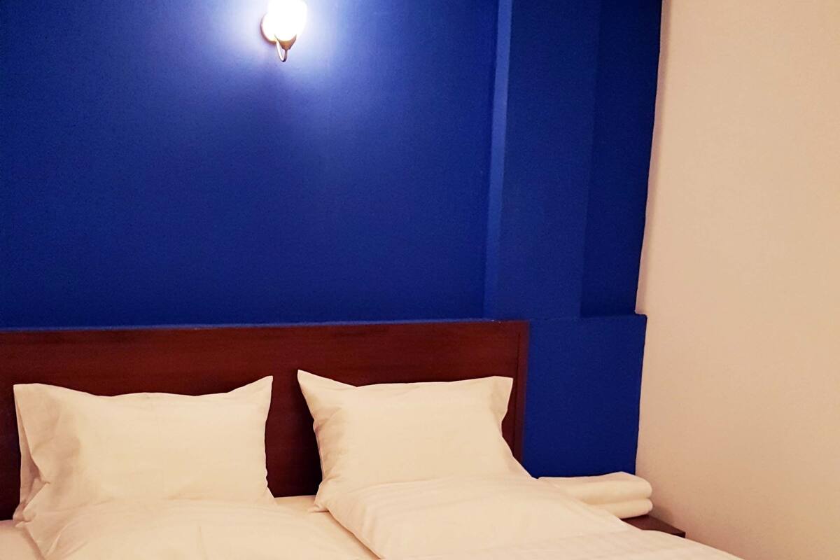 A neatly made bed with white linens and a wooden headboard in a room with blue walls.