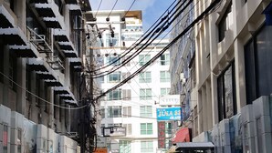 Uma rua estreita na cidade, com edifícios de ambos os lados, uma faixa de pedestres e algumas pessoas caminhando.