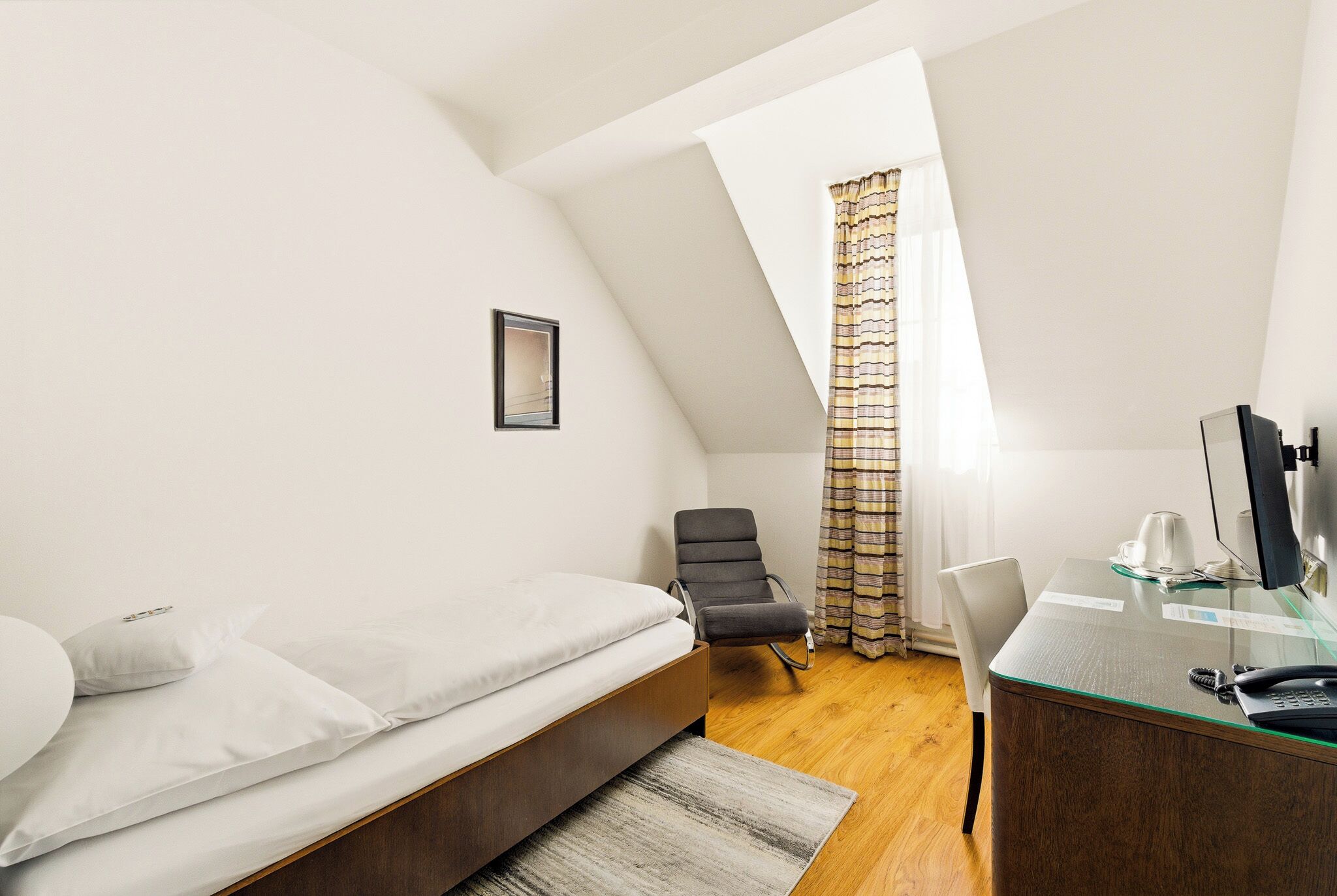 A bedroom with a bed, a desk, a chair, and a window with curtains.