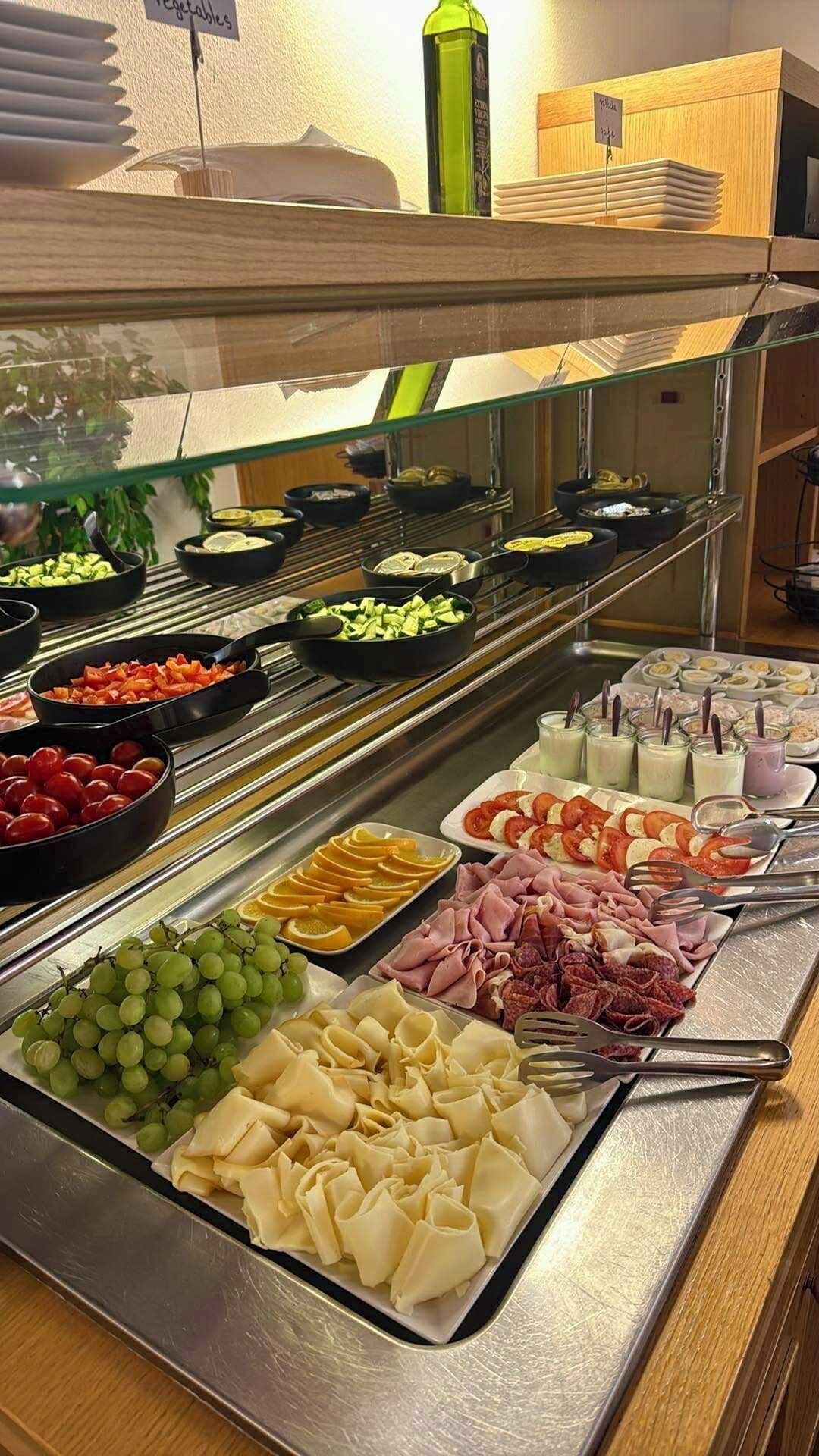 Un bufé con una variedad de alimentos, entre ellos frutas, verduras, quesos, carnes y ensaladas.