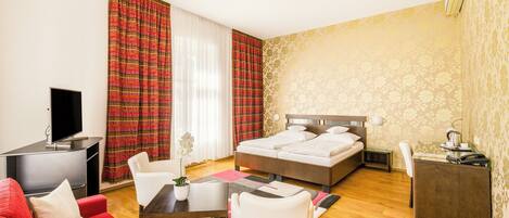 A hotel room with a bed, a desk, a TV, a red sofa, and a dining area.