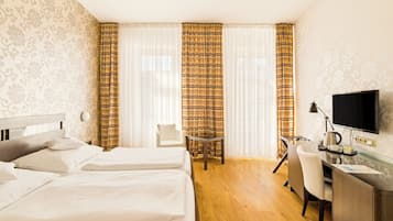 Une chambre d’hôtel avec deux lits, un bureau avec un ordinateur, une chaise et une télévision.