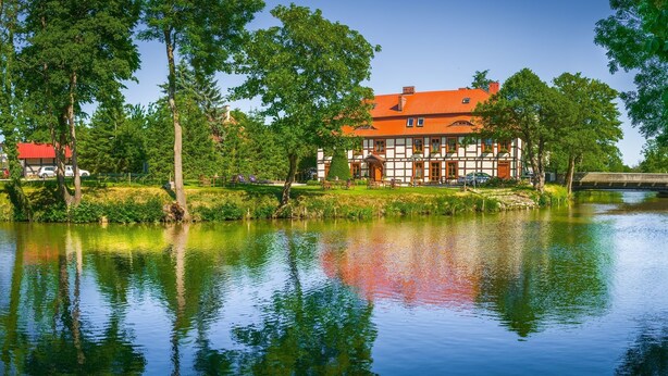 Una casa tradicional de entramado de madera junto a un río tranquilo, con un puente al fondo.