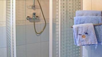 Um chuveiro envidraçado com chuveiro manual e porta-toalhas com toalhas.
