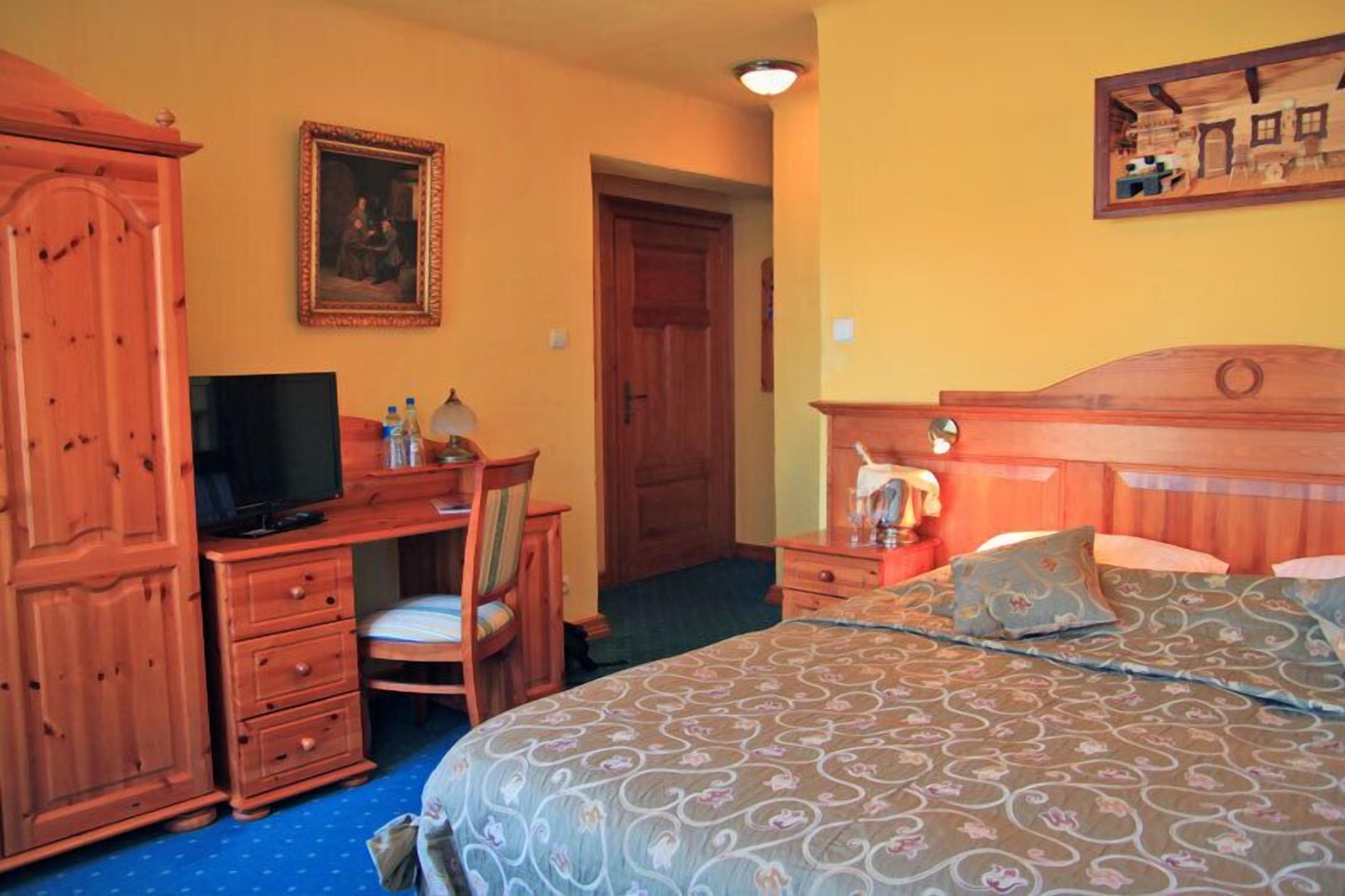 A bedroom with a bed, a desk, a chair, a television, and a wardrobe.