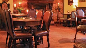 Un comedor con chimenea de ladrillo, vigas de madera en el techo y una mesa redonda con sillas.