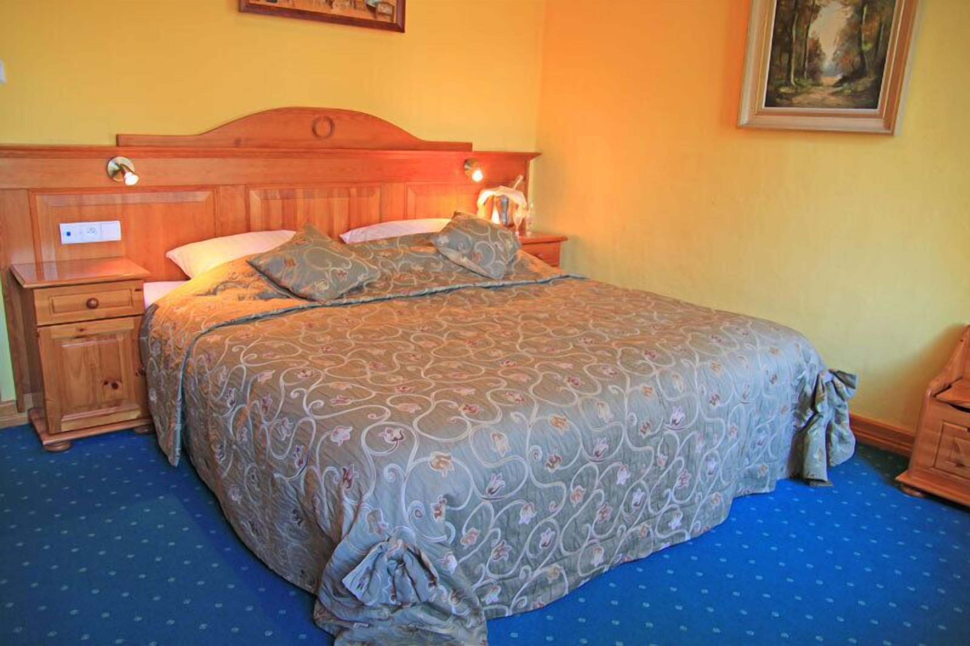 A bedroom with a wooden headboard, a bed with patterned bedding, a nightstand with a lamp, and a dresser.